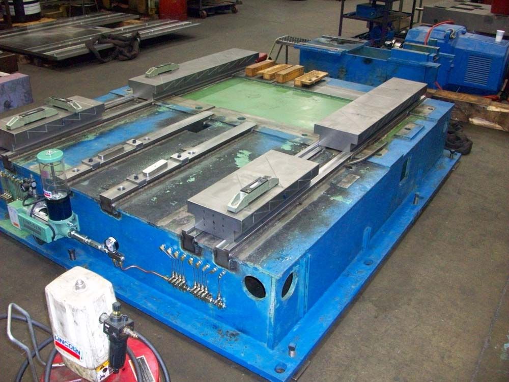 Blue industrial machine on a factory floor with a large metal platform and control box