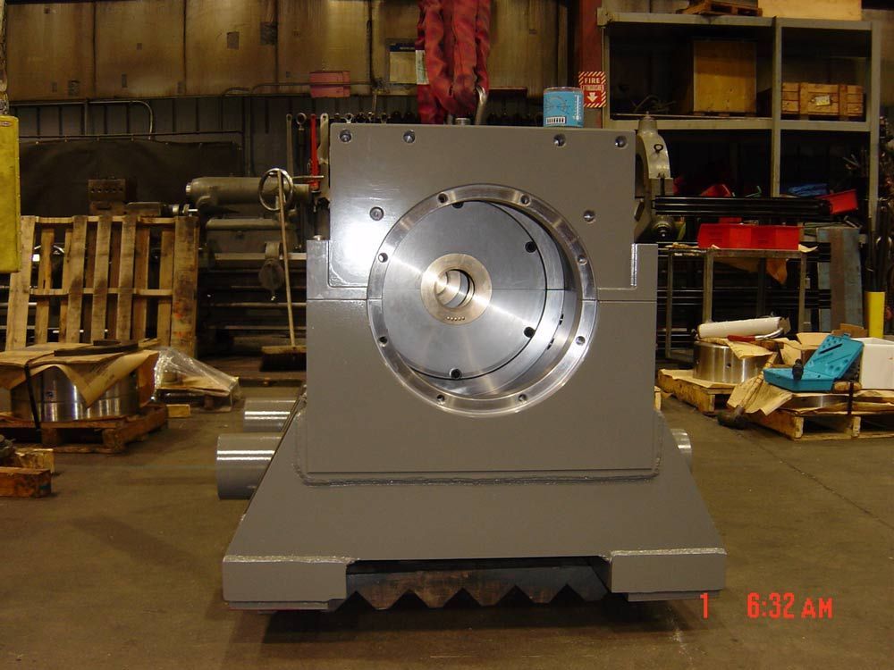 Large gray industrial machine with a circular metal opening in a warehouse workshop.