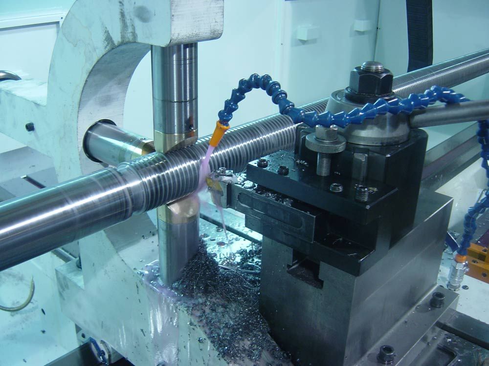 Metal rod being machined on a lathe with cutting fluid spraying onto the tool and workpiece.