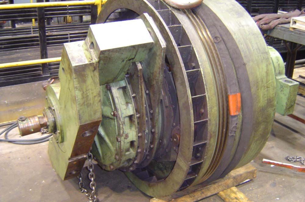 Large industrial metal wheel or drum assembly with green housing and black bands in a workshop.