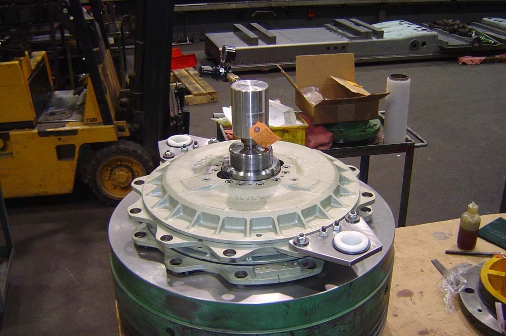 Large industrial machine component on a workshop floor, with tools and a forklift in the background.