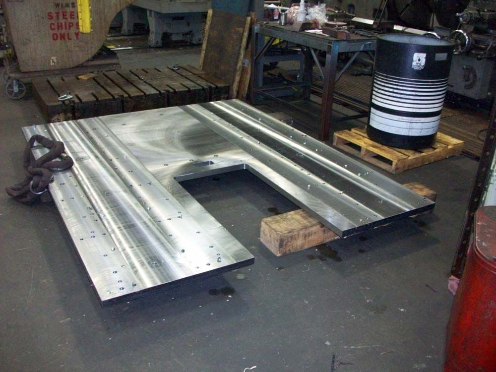 Large metal sheet structure on a workshop floor beside a wooden pallet and striped barrel.