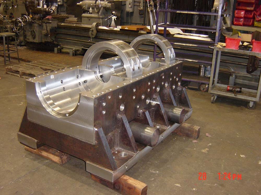 Large metal industrial machine component in a workshop, with polished silver cylinders on a dark base.