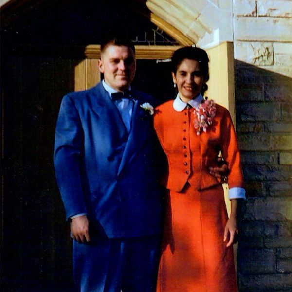 Two people standing together outside, wearing bright blue and orange formal outfits.
