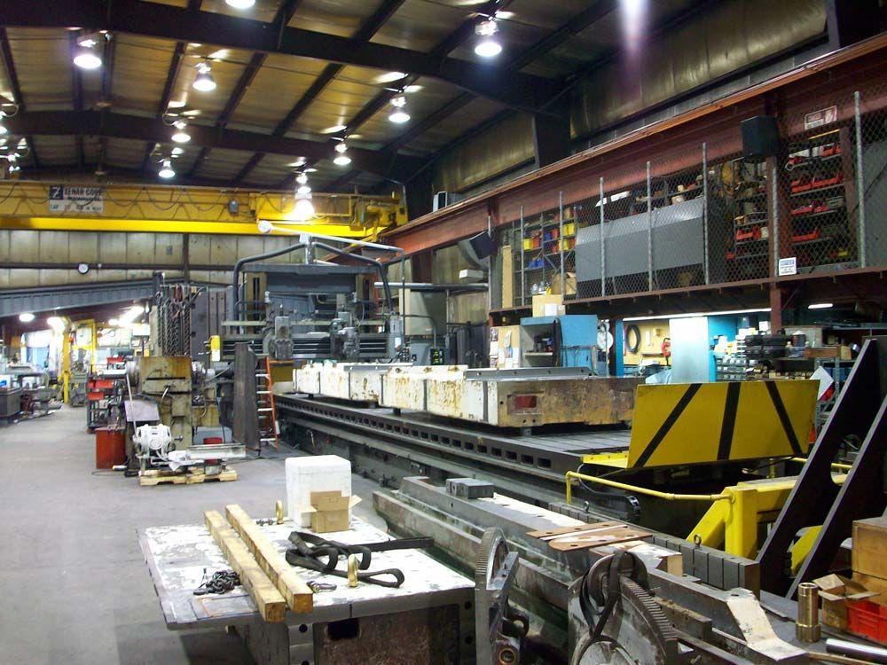 Large industrial workshop with machinery, workbenches, and overhead cranes in a warehouse-like factory.