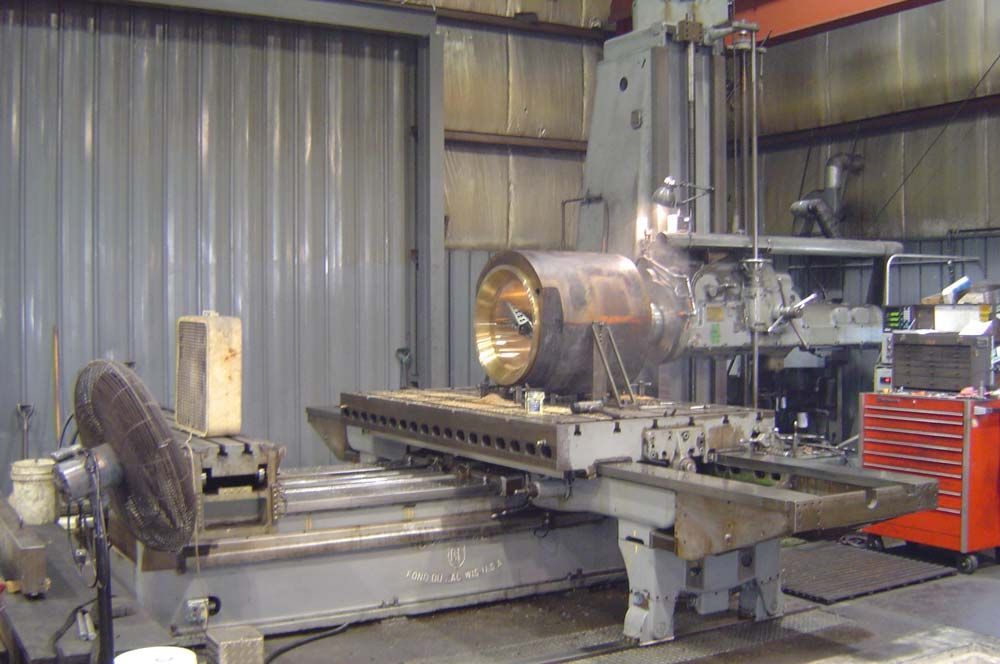 Industrial machine in a workshop, with a large metal lathe and control panels against corrugated walls.