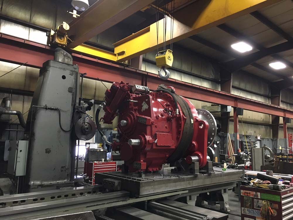 Large red industrial machine in a factory workshop with overhead cranes and metal beams