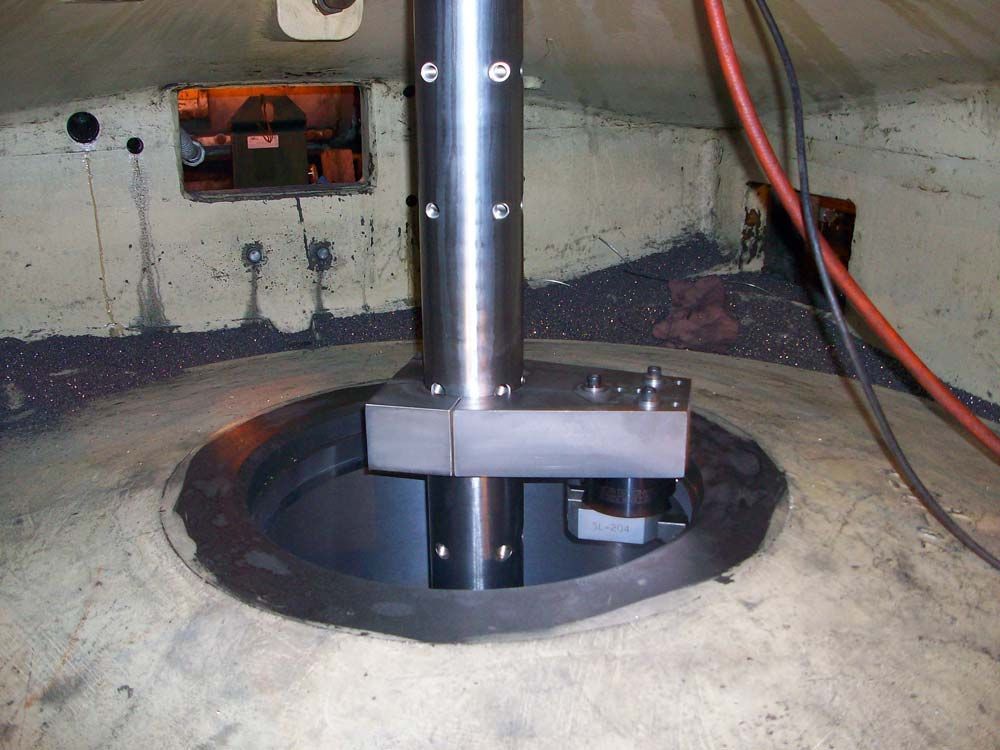 Black metal pipe mounted through a circular floor opening in a concrete room