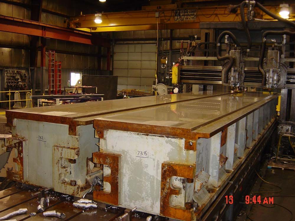 Large industrial machine in a factory with metal panels and a worker in the background