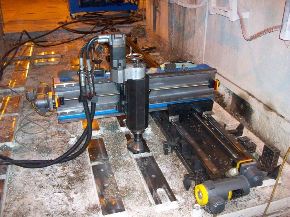 Compact CNC machine setup on a dirty workshop floor with blue rails, black motor, and cables