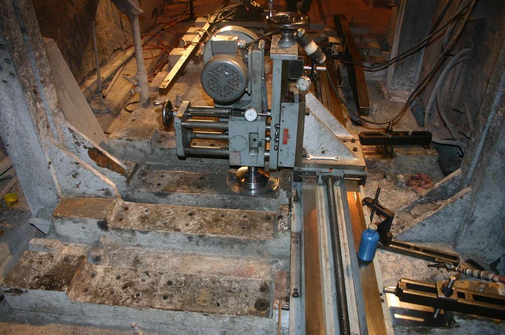 Industrial tunnel with a rail-mounted machine and metal tracks in a rocky, unfinished underground shaft