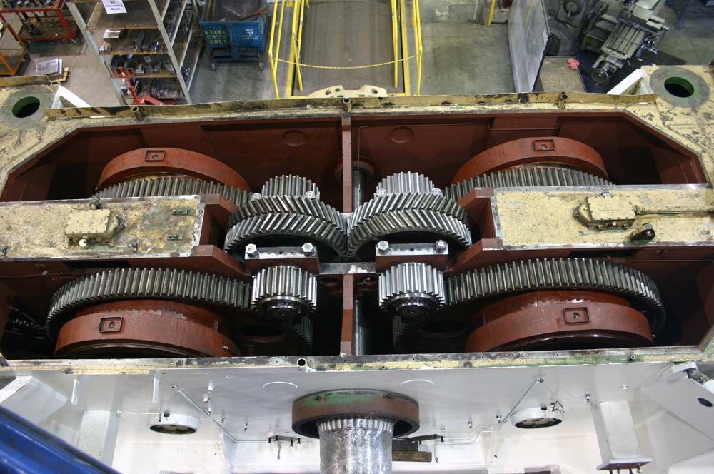 Industrial gearbox with large red gears and black helical gears in a factory assembly setting
