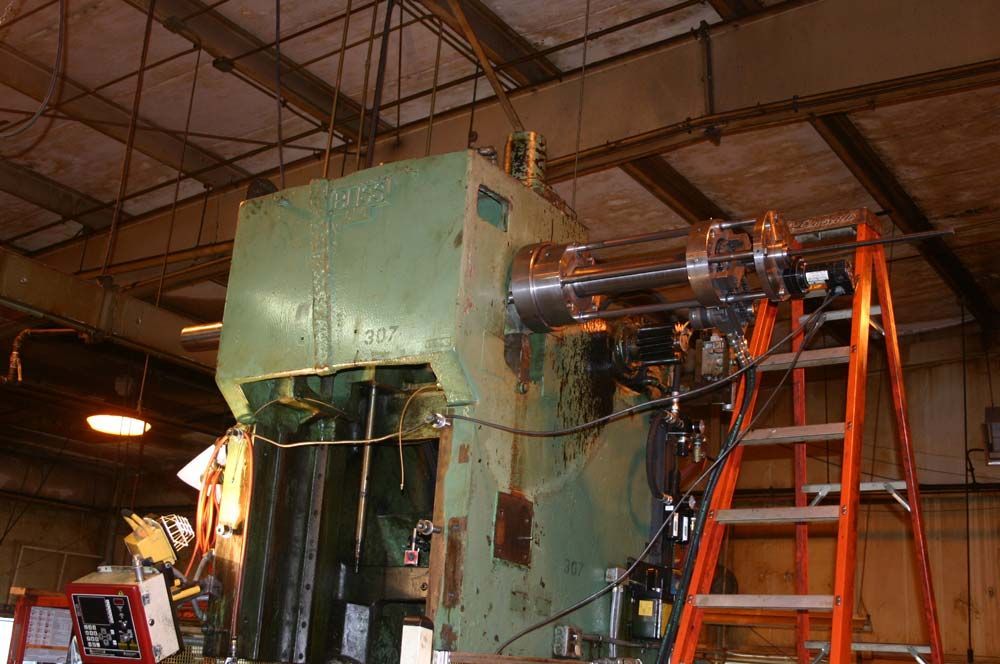 Large industrial machine in a warehouse, with exposed wiring and a ladder beside it.