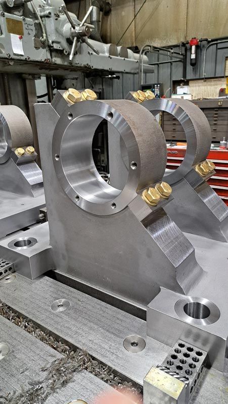 Machined metal fixture with a large circular opening in an industrial workshop, with brass clamps and gray surfaces