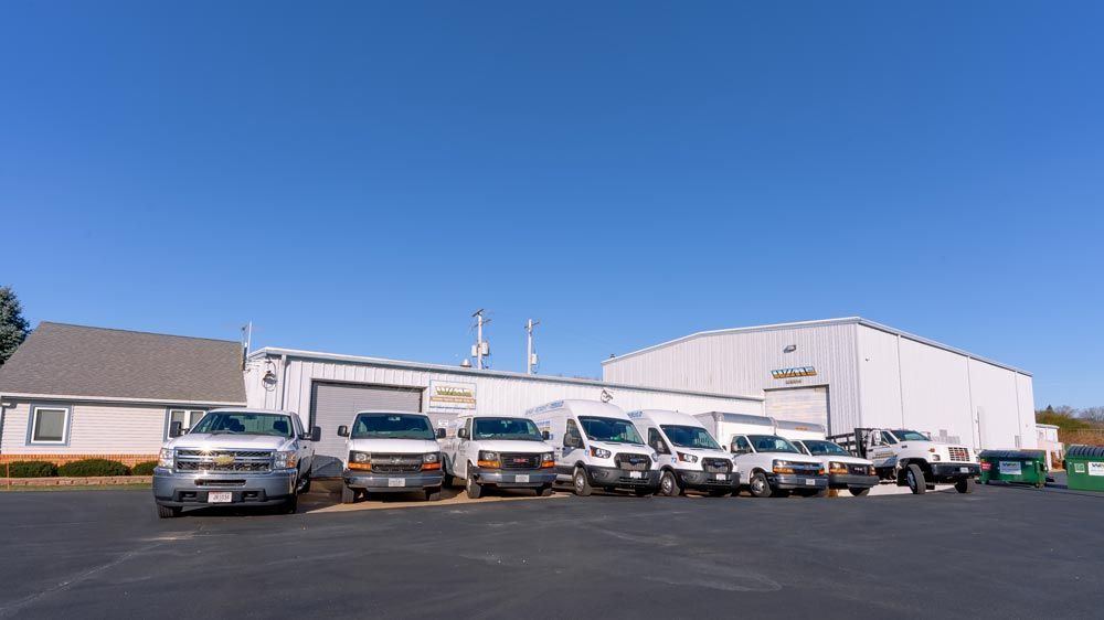 White commercial building with a row of parked service trucks on a sunny day