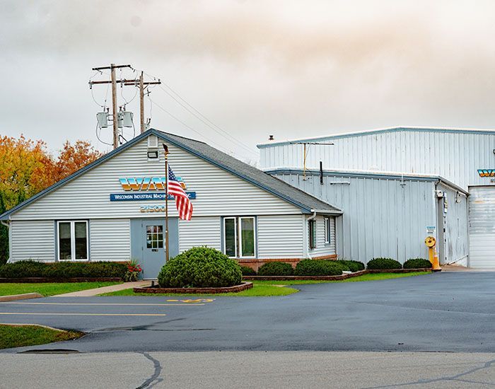 Small white industrial office building with an American flag and attached warehouse on a cloudy day