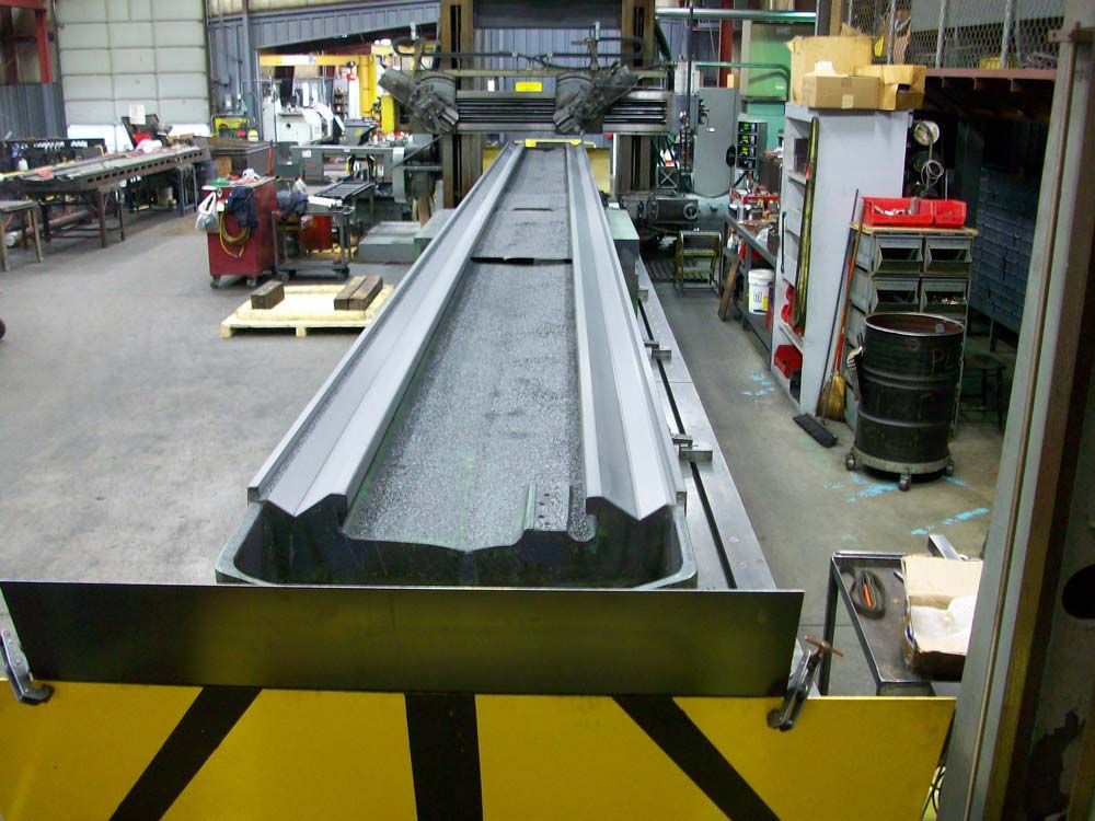Industrial factory floor with a long metal conveyor or chute assembly on yellow support beams