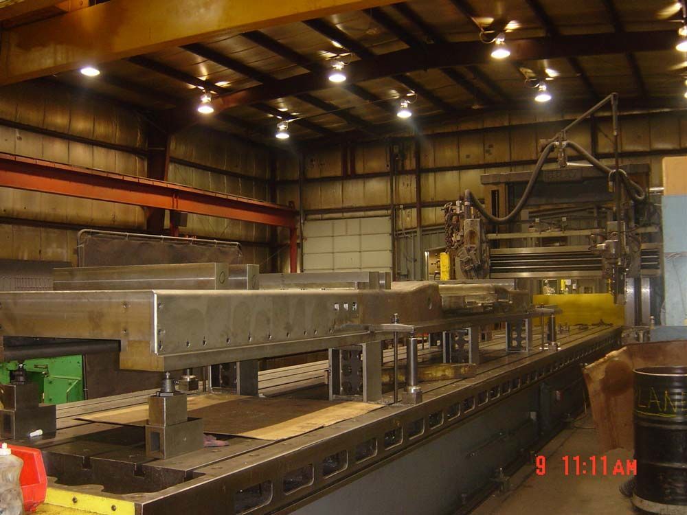 Large industrial machine in a factory workshop with metal framework and overhead crane.