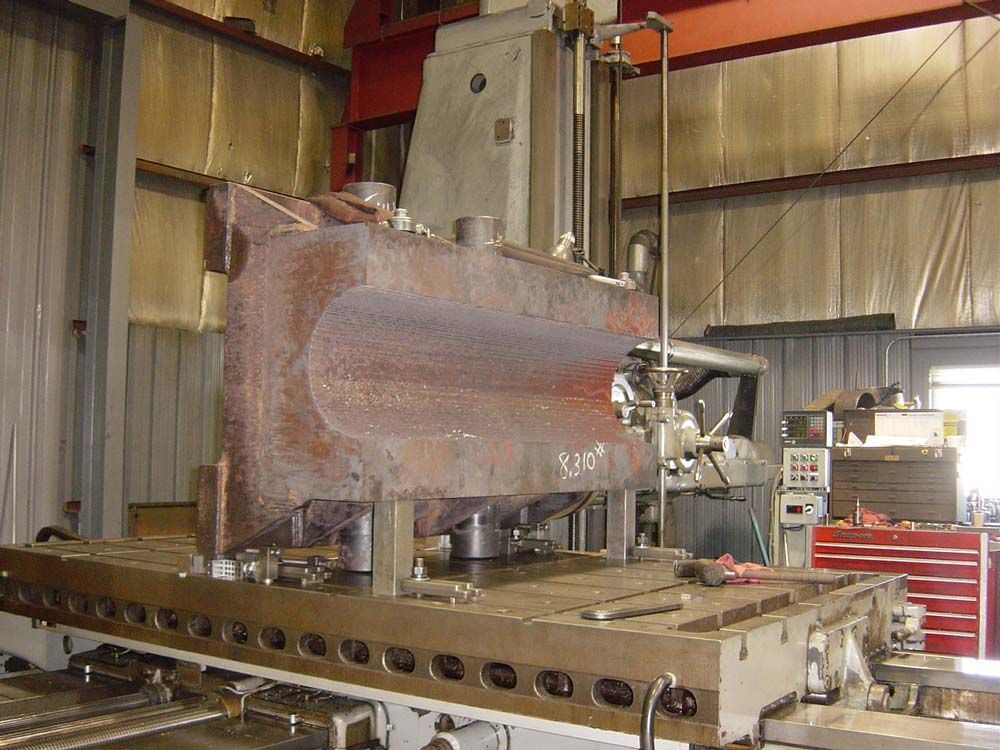 Rusty industrial machine in a workshop, mounted on a metal base with surrounding equipment.