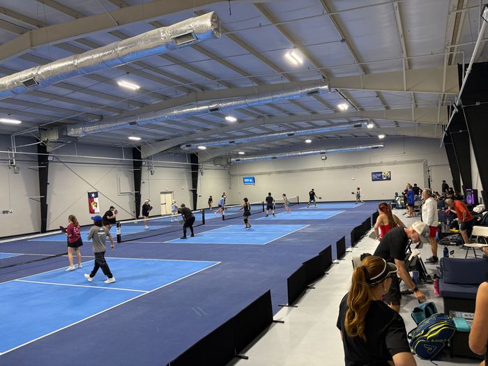 Indoor gymnastics competition in a large blue-matted arena with athletes and spectators.