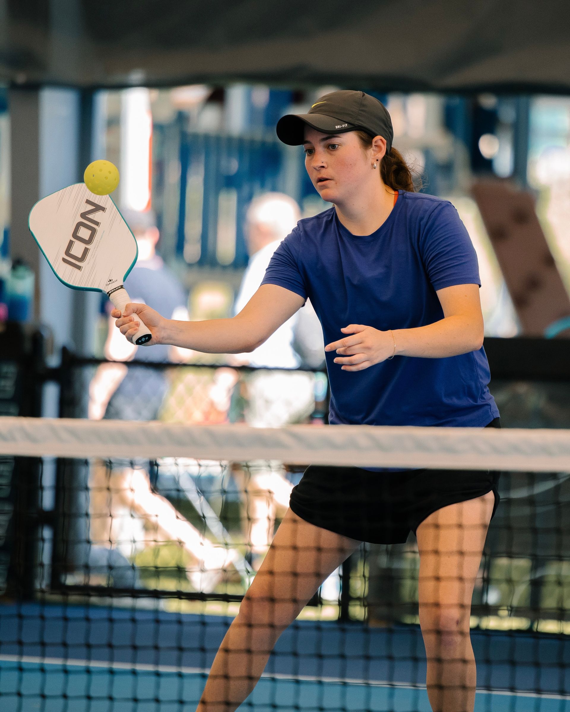 Tennis player in blue shirt and black cap preparing to hit a ball on an indoor court