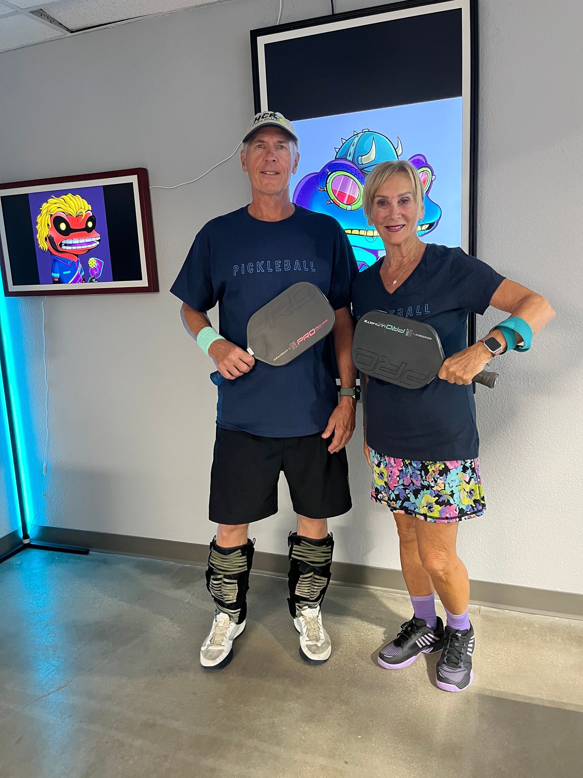 Two people posing with trophies in front of wall-mounted screens in an indoor event space
