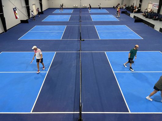 Indoor pickleball courts with players in blue-floored gymnasium