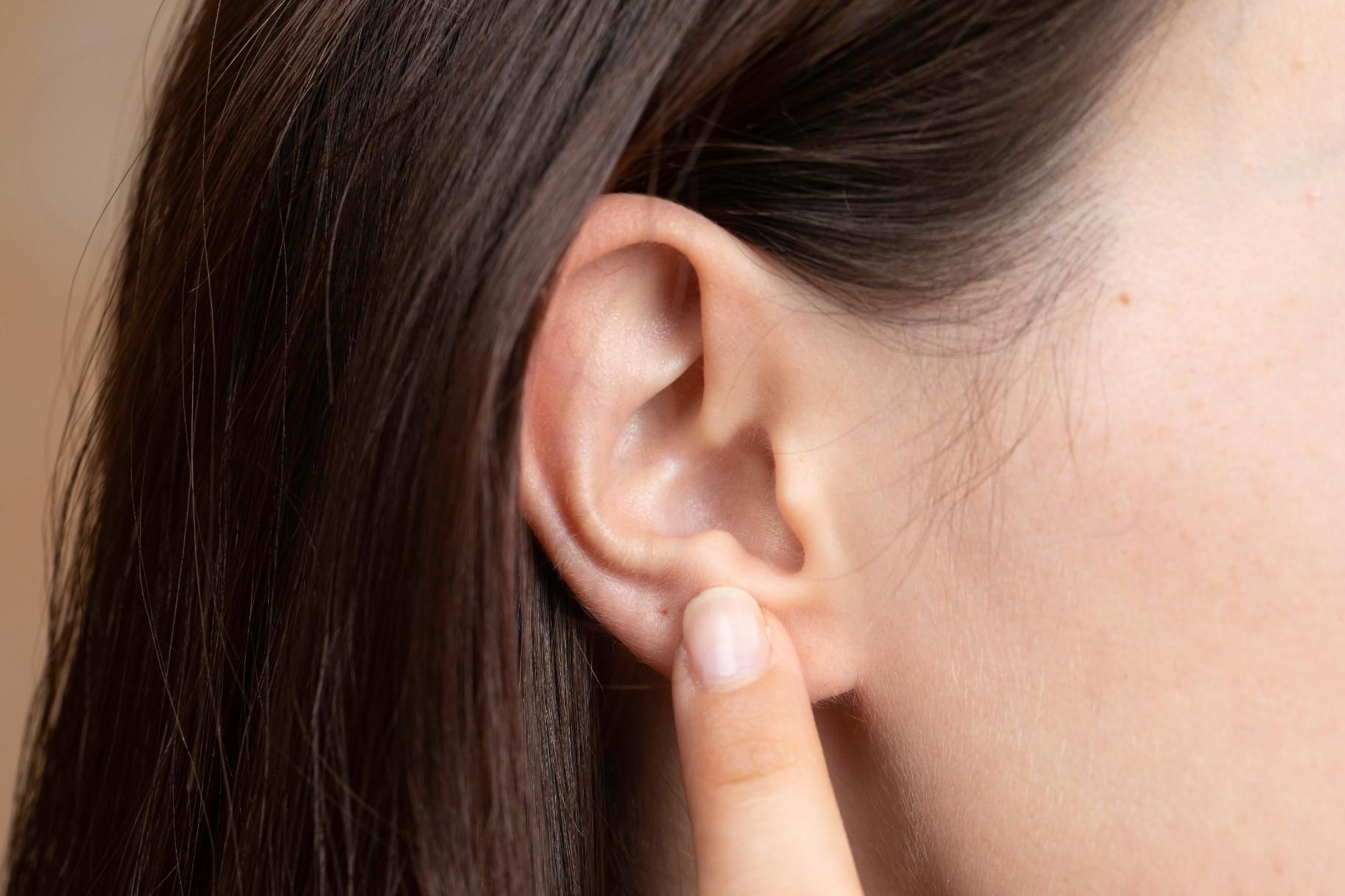 A Woman is Touching Her Ear With Her Finger — Clayton Hearing in Pialba, QLD