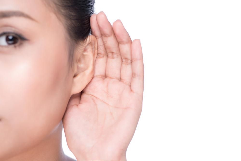 A Woman is Holding Her Hand to Her Ear to Hear Something — Clayton Hearing in Pialba, QLD
