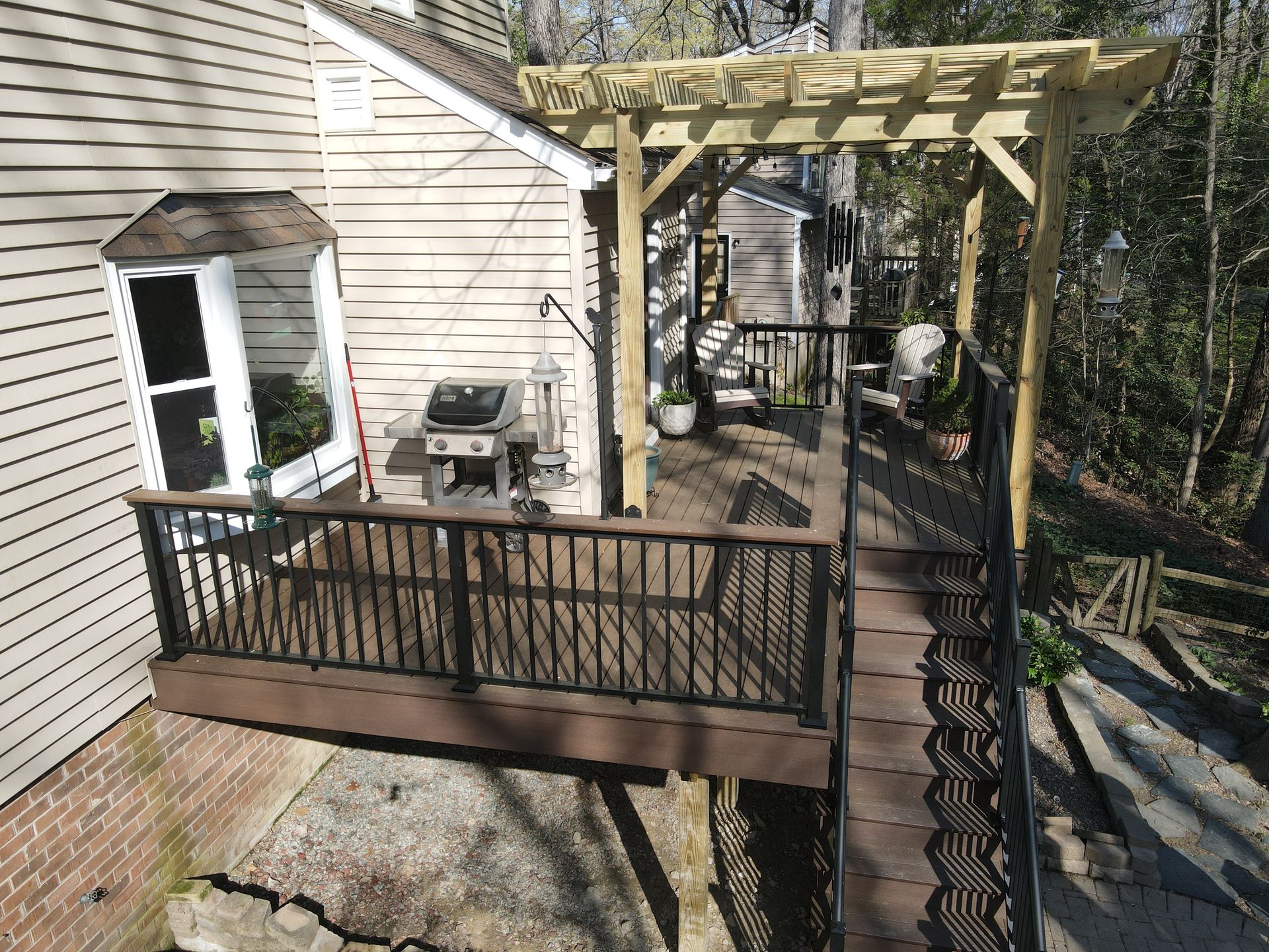 Wooden backyard deck with pergola attached to a house, overlooking a wooded yard.