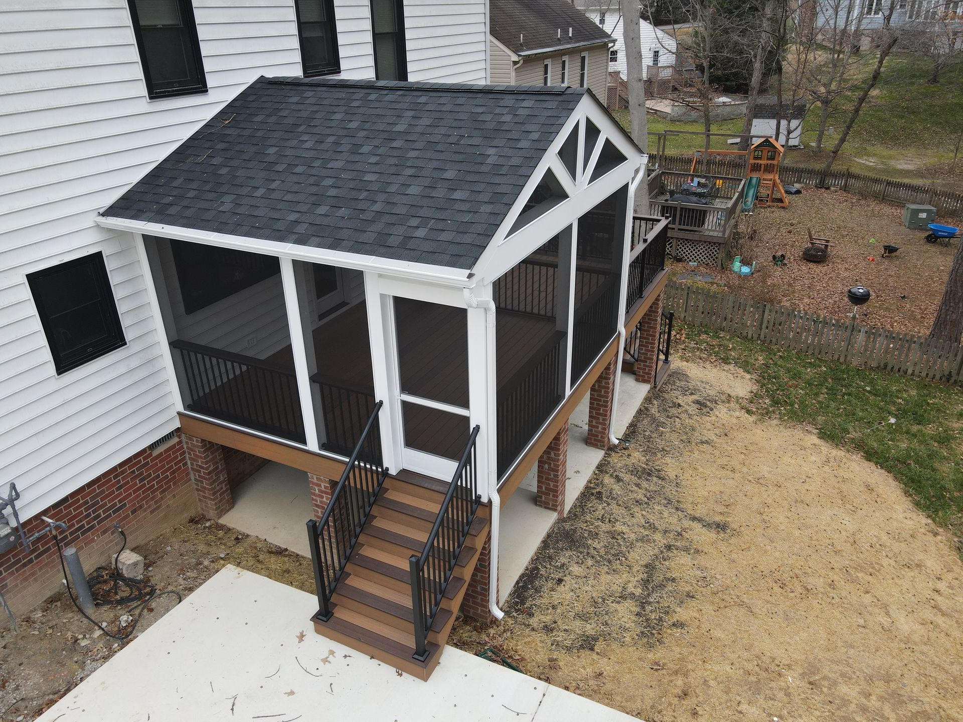 Small screened porch with black roof and white trim attached to a house, viewed from the yard