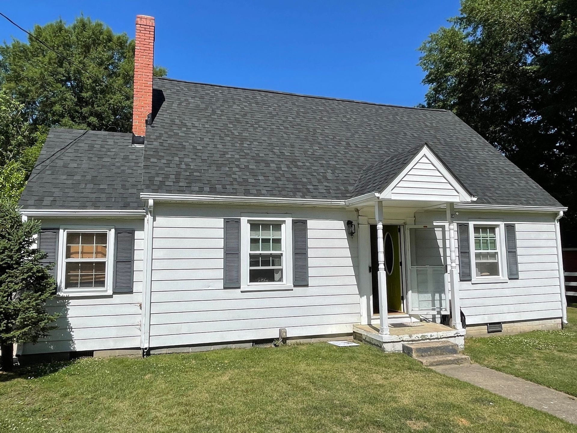 White house with dark roof, red chimney, and front porch on a sunny day
