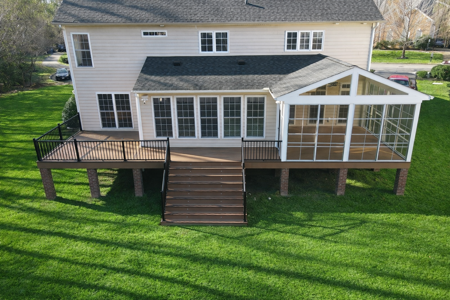 Rear view of a two-story house with a deck, stairs, and enclosed sunroom overlooking a grassy yard