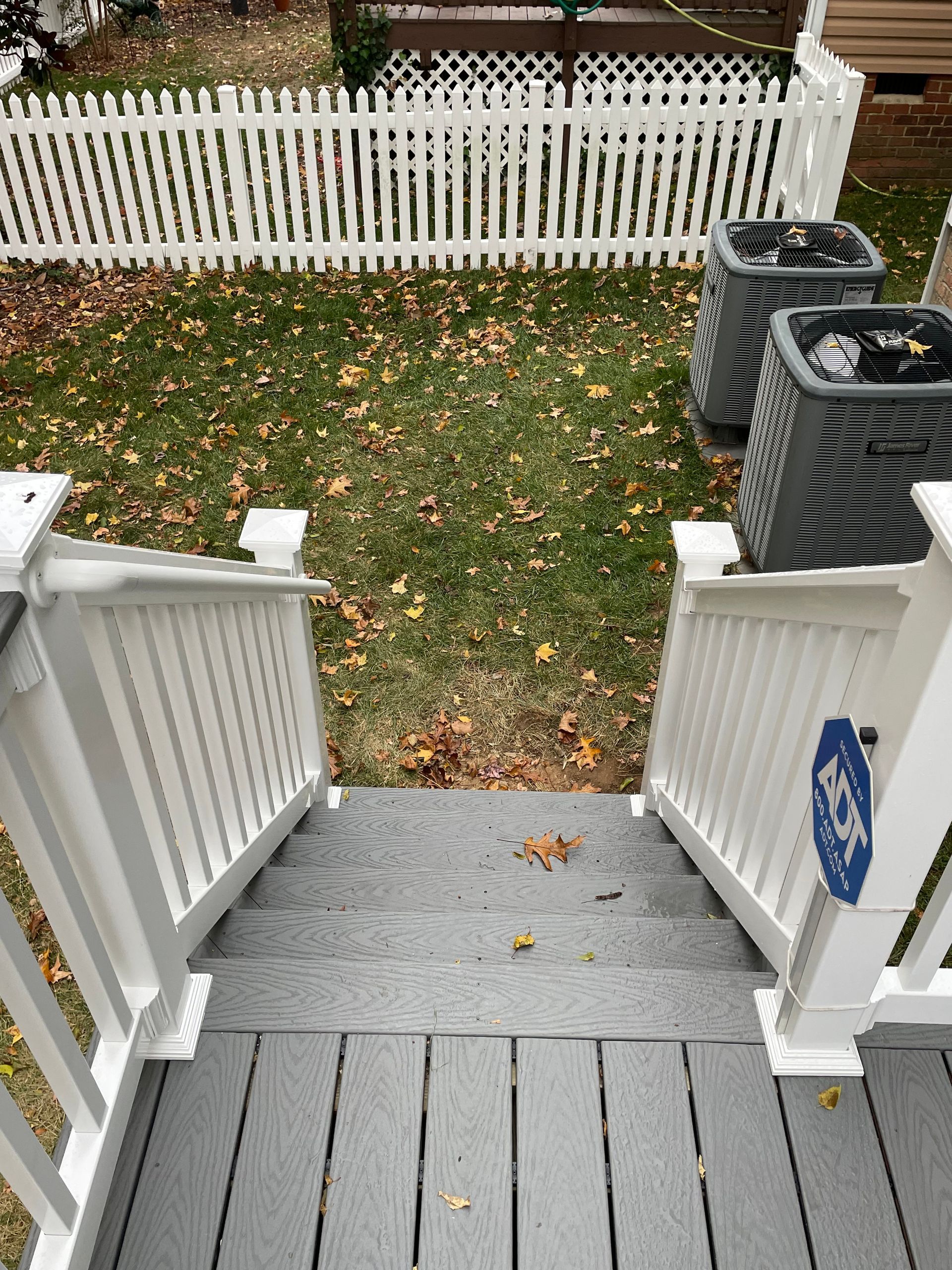 Front porch steps leading to a grassy yard and white picket fence with autumn leaves.
