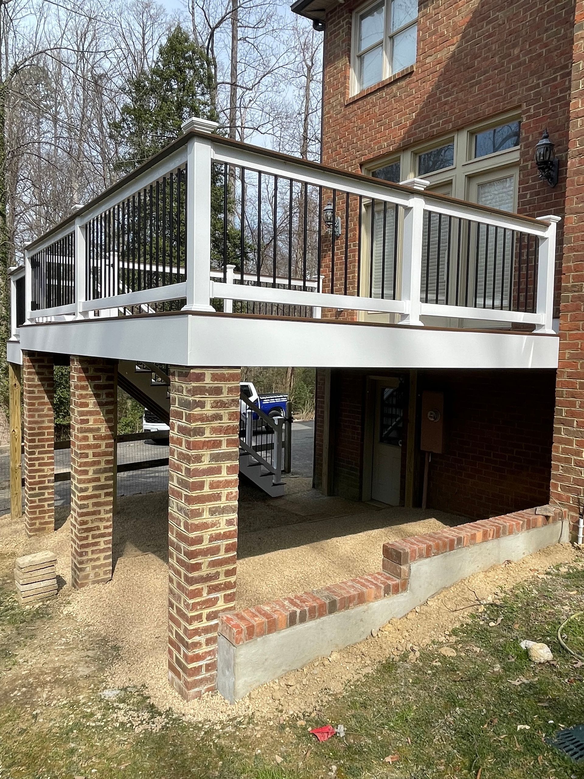 Brick house with elevated white-railed deck and brick support pillars over a shaded lower patio