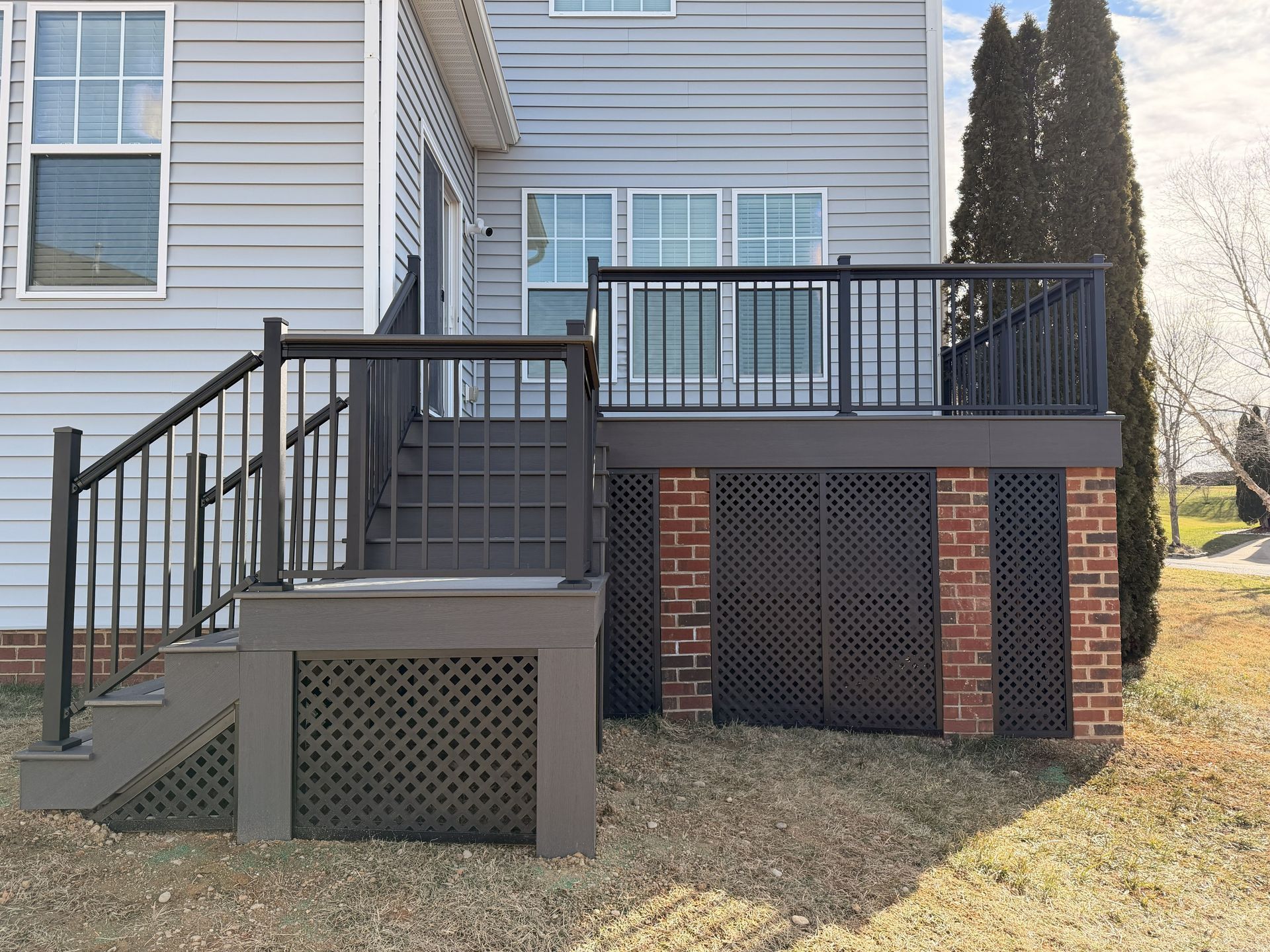 Raised wooden deck with black railings and stairs on the back of a gray house