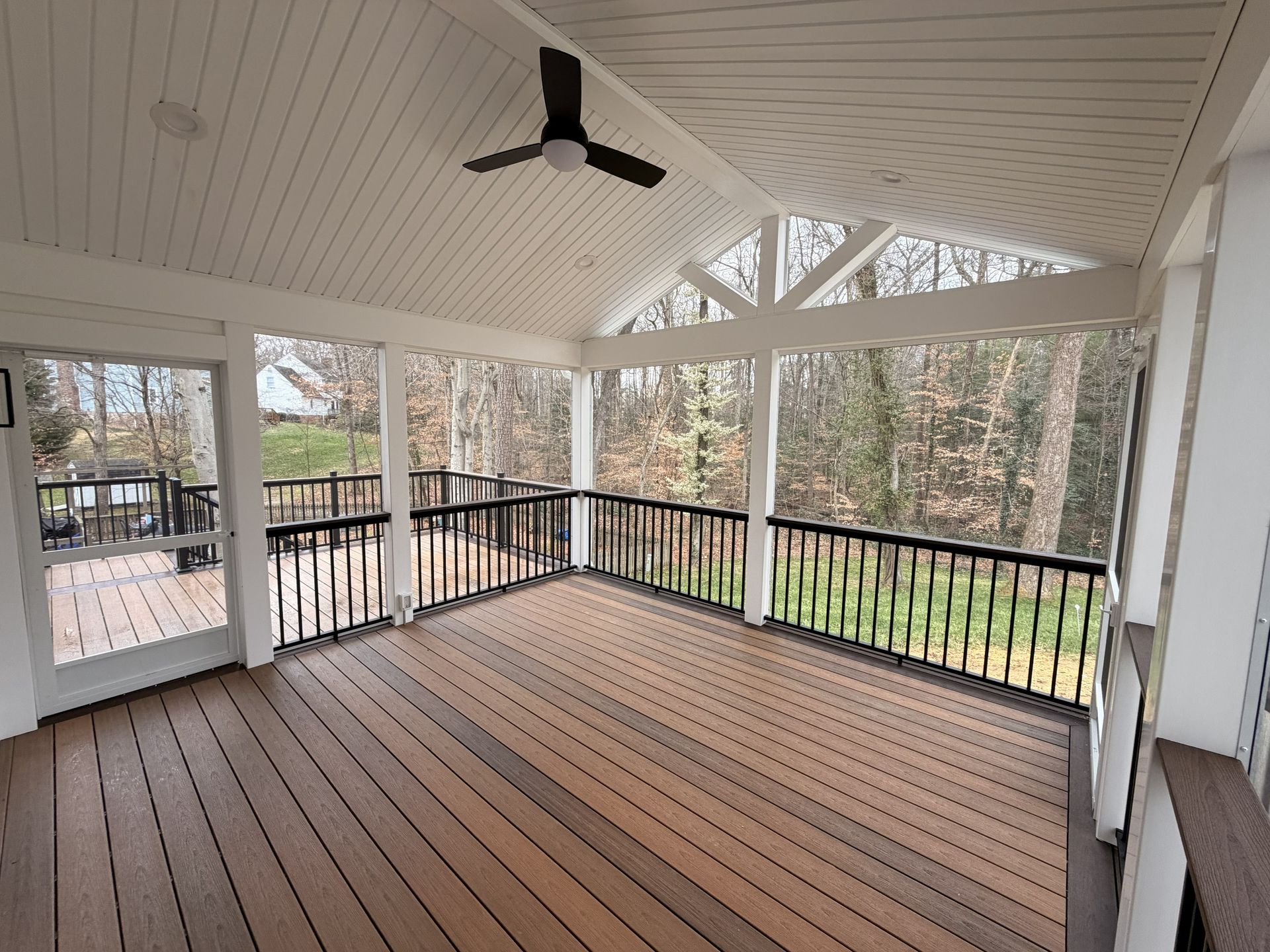 Covered porch with wood floor, white ceiling, black railings, and a ceiling fan overlooking trees.