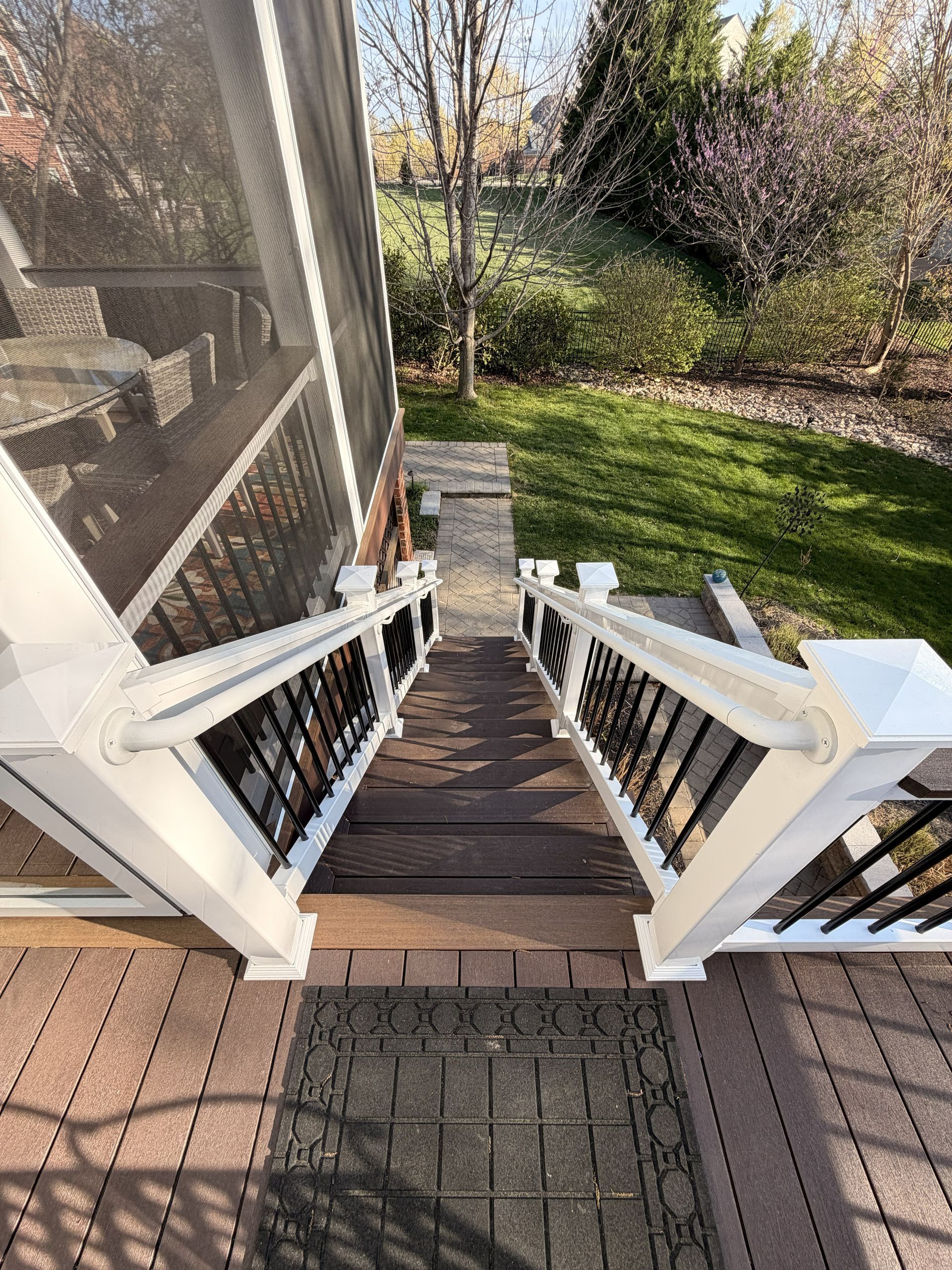 Front porch stairs with white railings leading down to a grassy yard and garden.