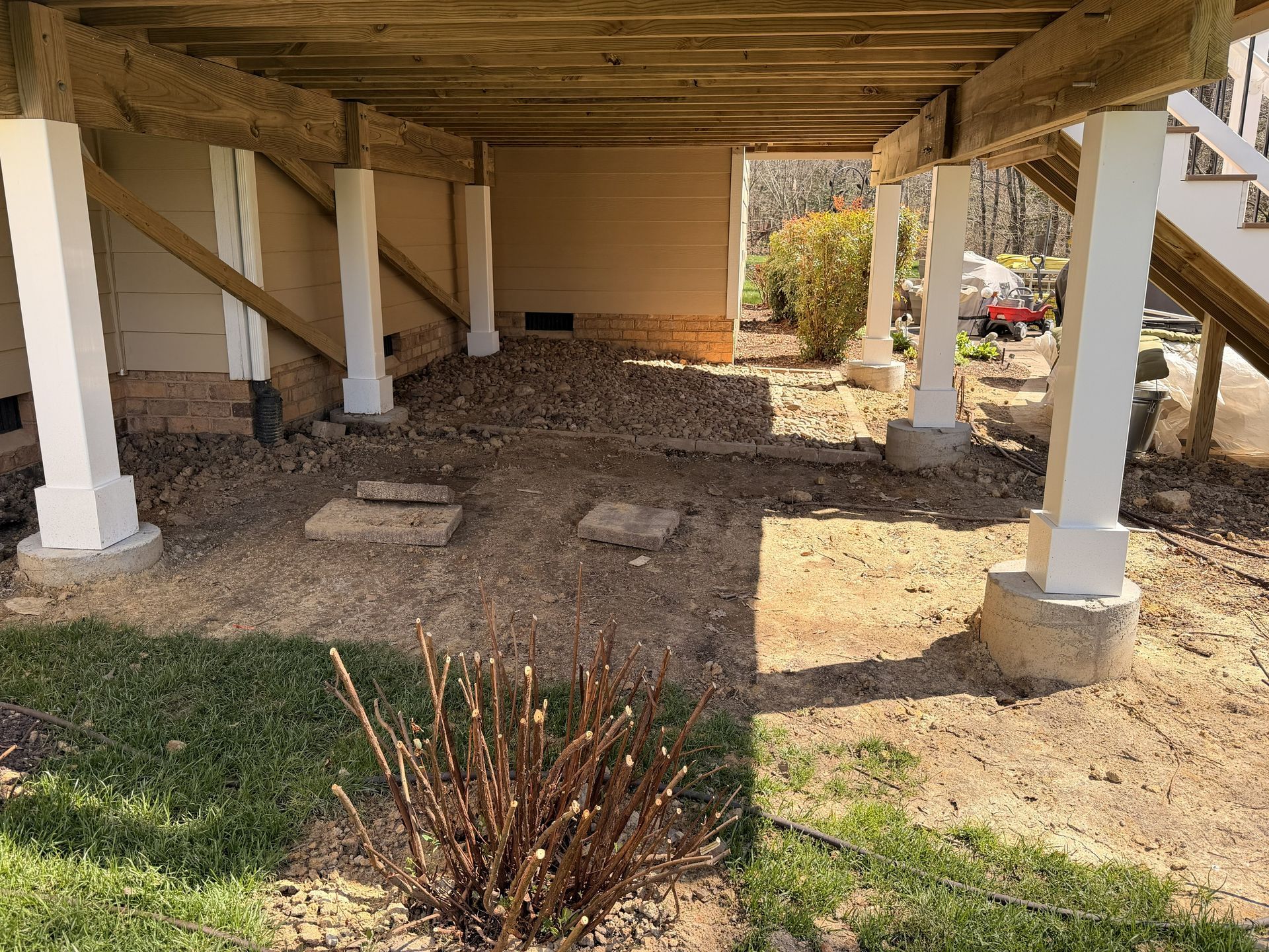 Under raised house, white support posts and gravel ground in shaded crawlspace area