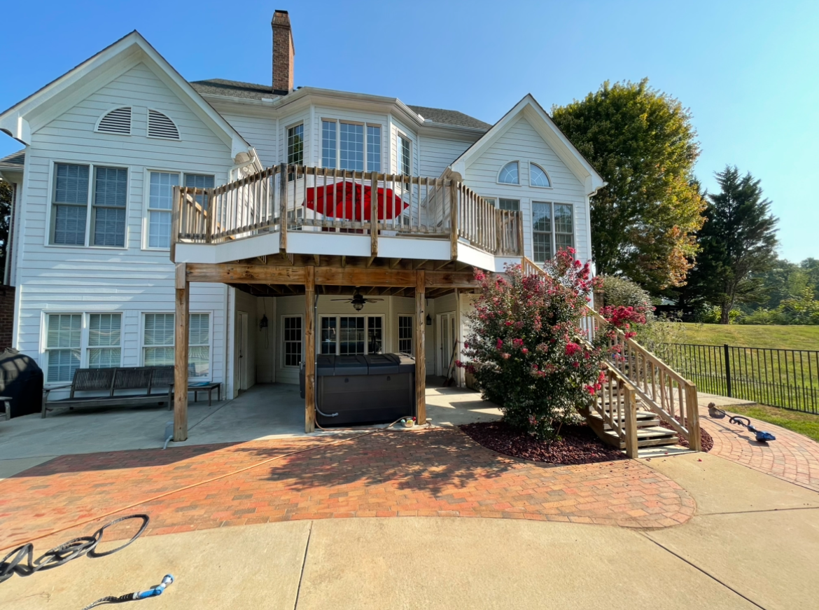 White Victorian-style house with a front balcony, red chairs, and a driveway in bright sunlight