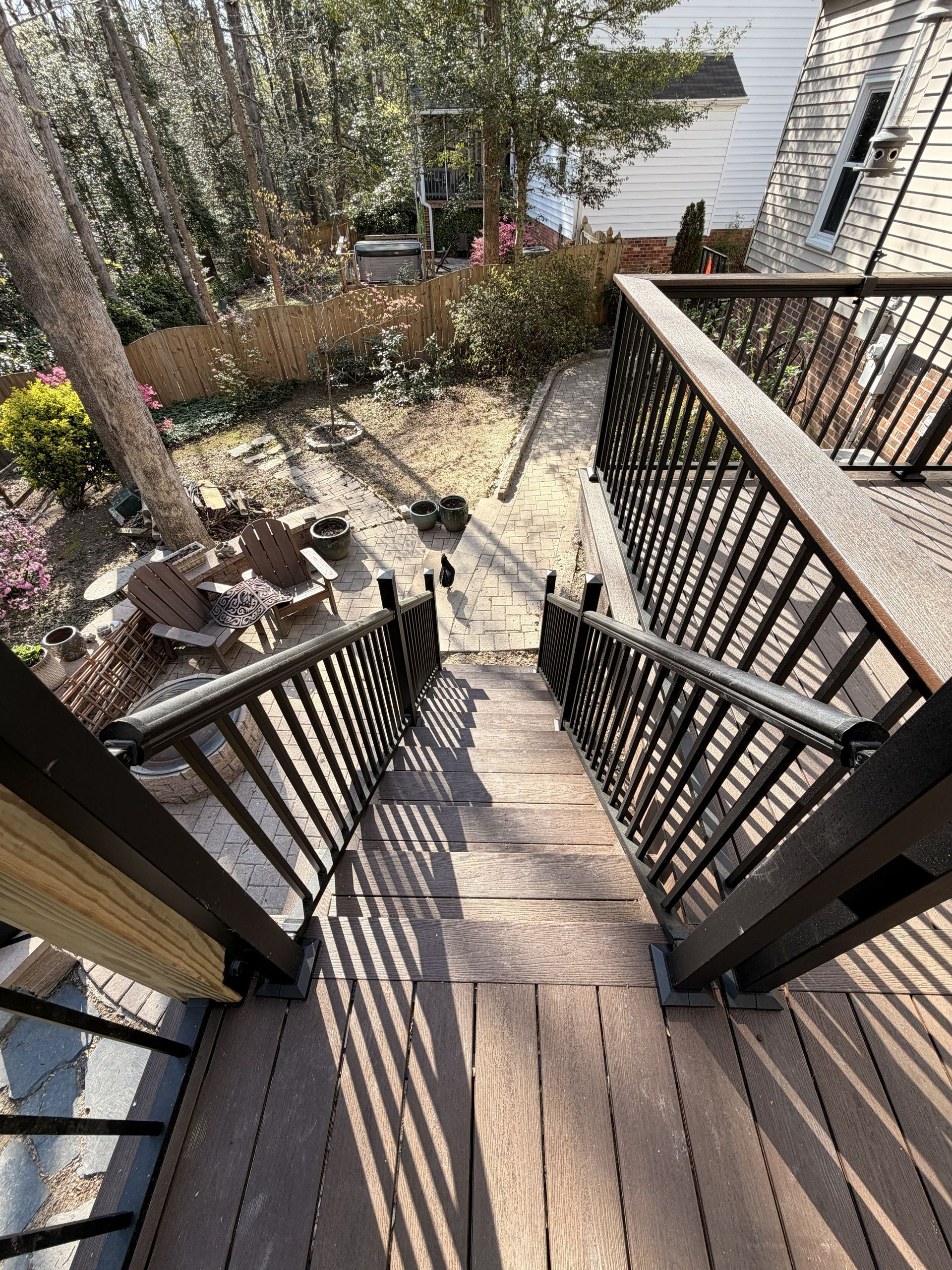 Wooden outdoor staircase descending to a patio with tables and chairs in a sunny yard