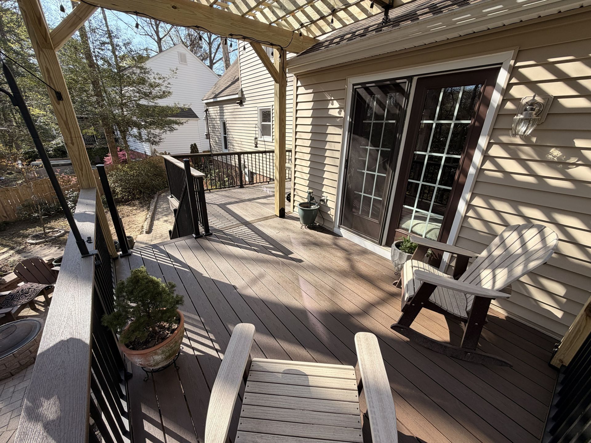 Wooden backyard deck with railing, potted plants, chair, and sliding glass door in sunlight