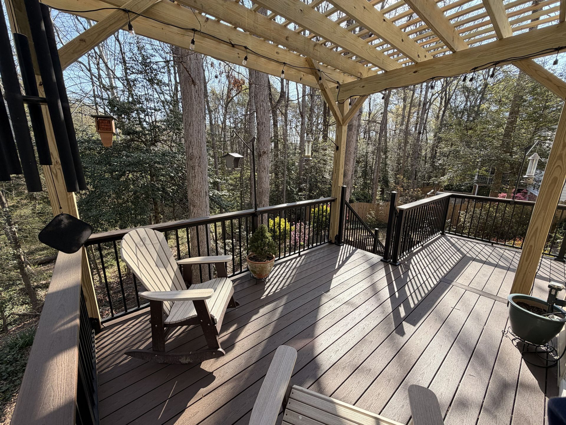 Covered wooden deck with chairs, railing, and potted plant overlooking a wooded yard