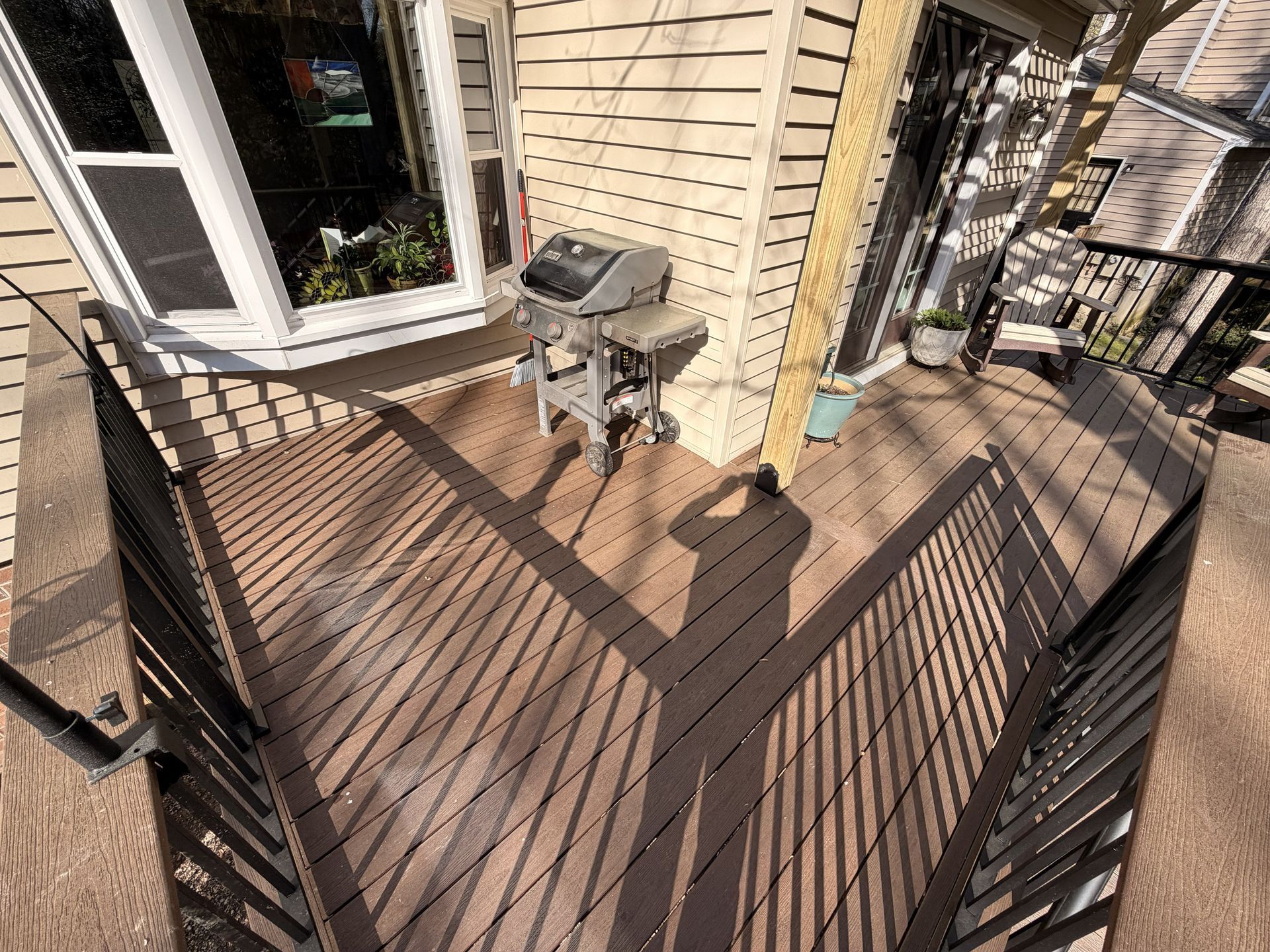 Wooden deck with a grill beside a house and black metal railings in bright sunlight