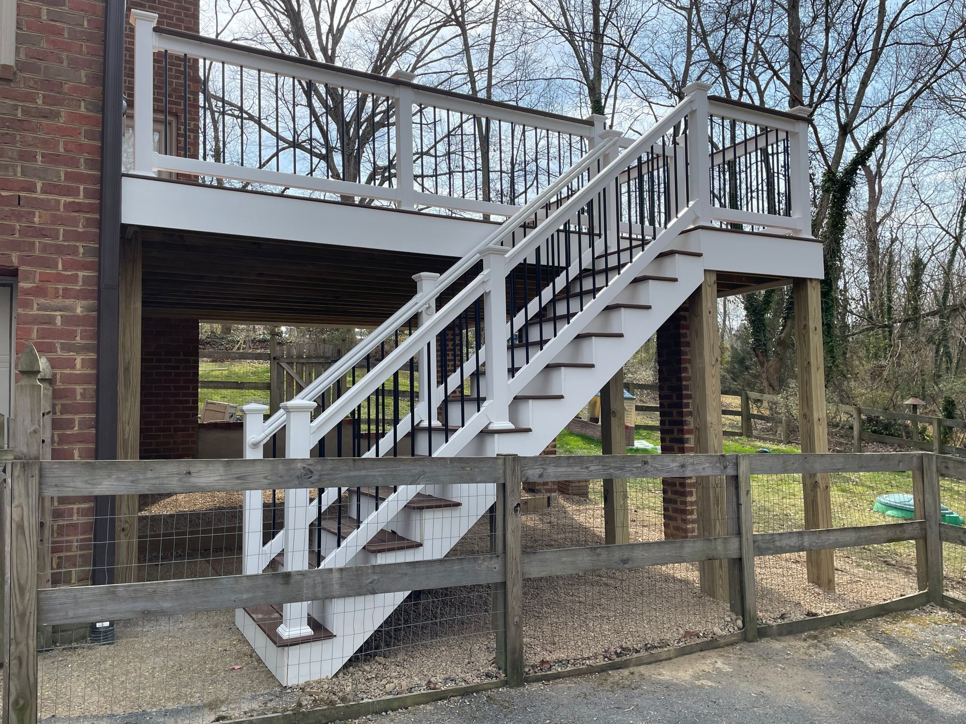 White wooden staircase leading to an elevated deck on a brick house, with a fenced yard below.