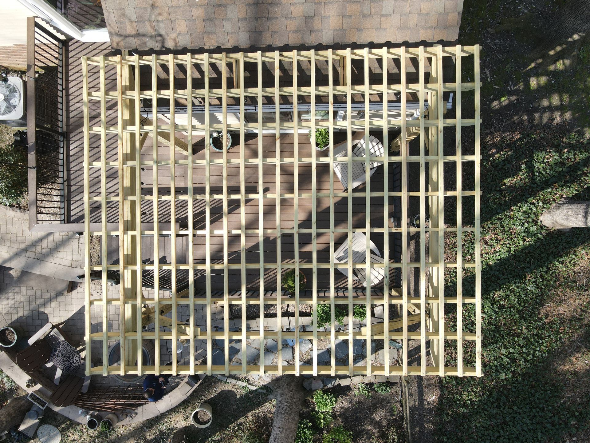 Overhead view of a yellow wooden pergola frame being built beside a house and lawn