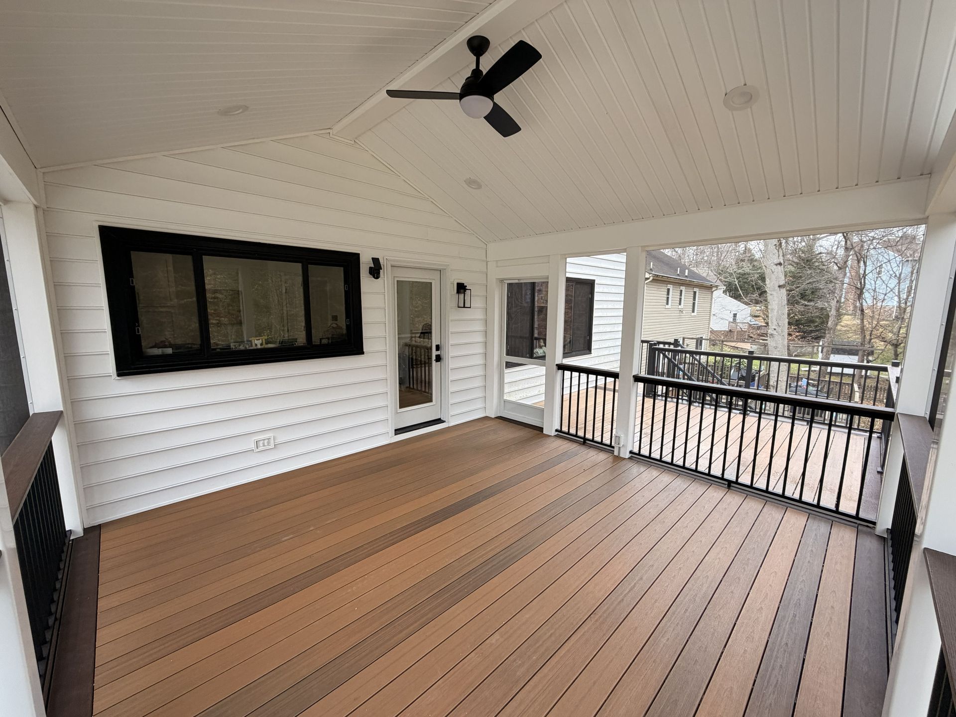 Covered porch with wood deck, white siding, black railings, and a ceiling fan, viewed toward the yard.