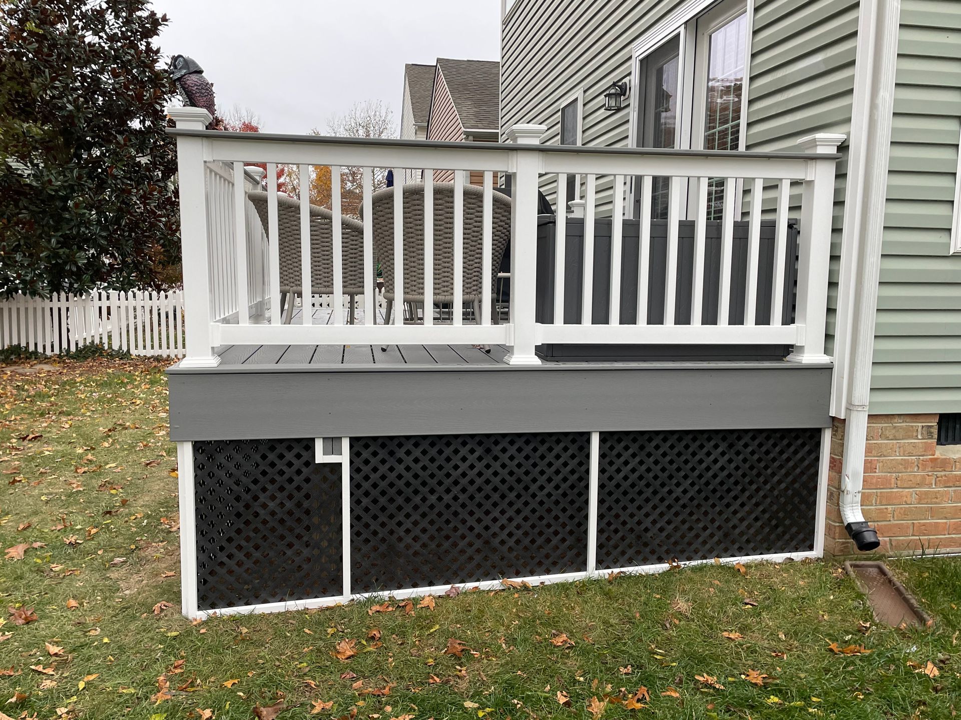 Back porch with white railing and gray skirting above a black lattice foundation on a grassy yard