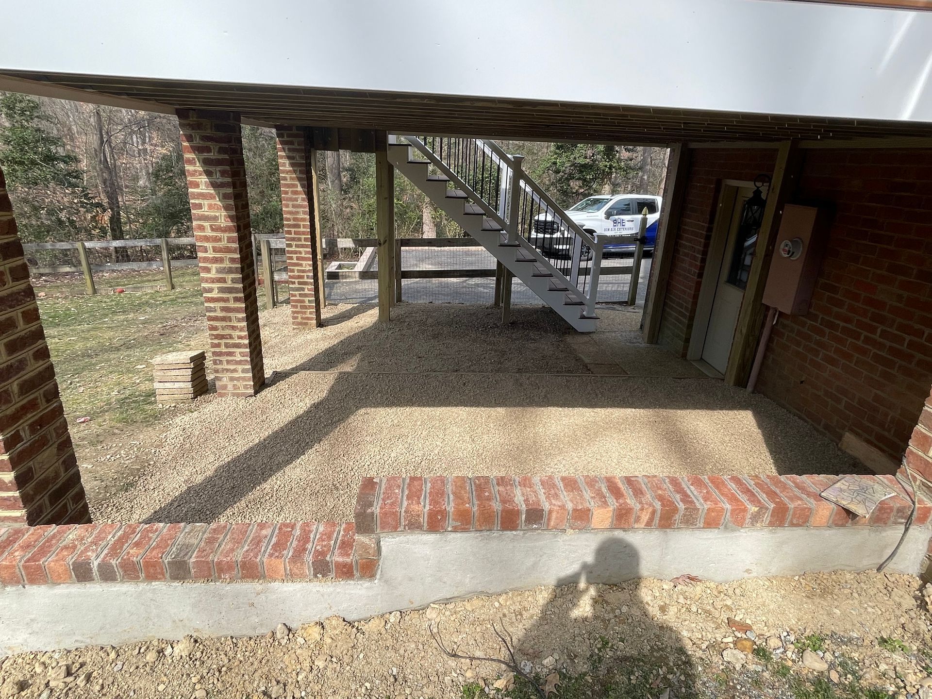 Covered outdoor patio with brick walls, concrete floor, stairs, and a parked car in the background.