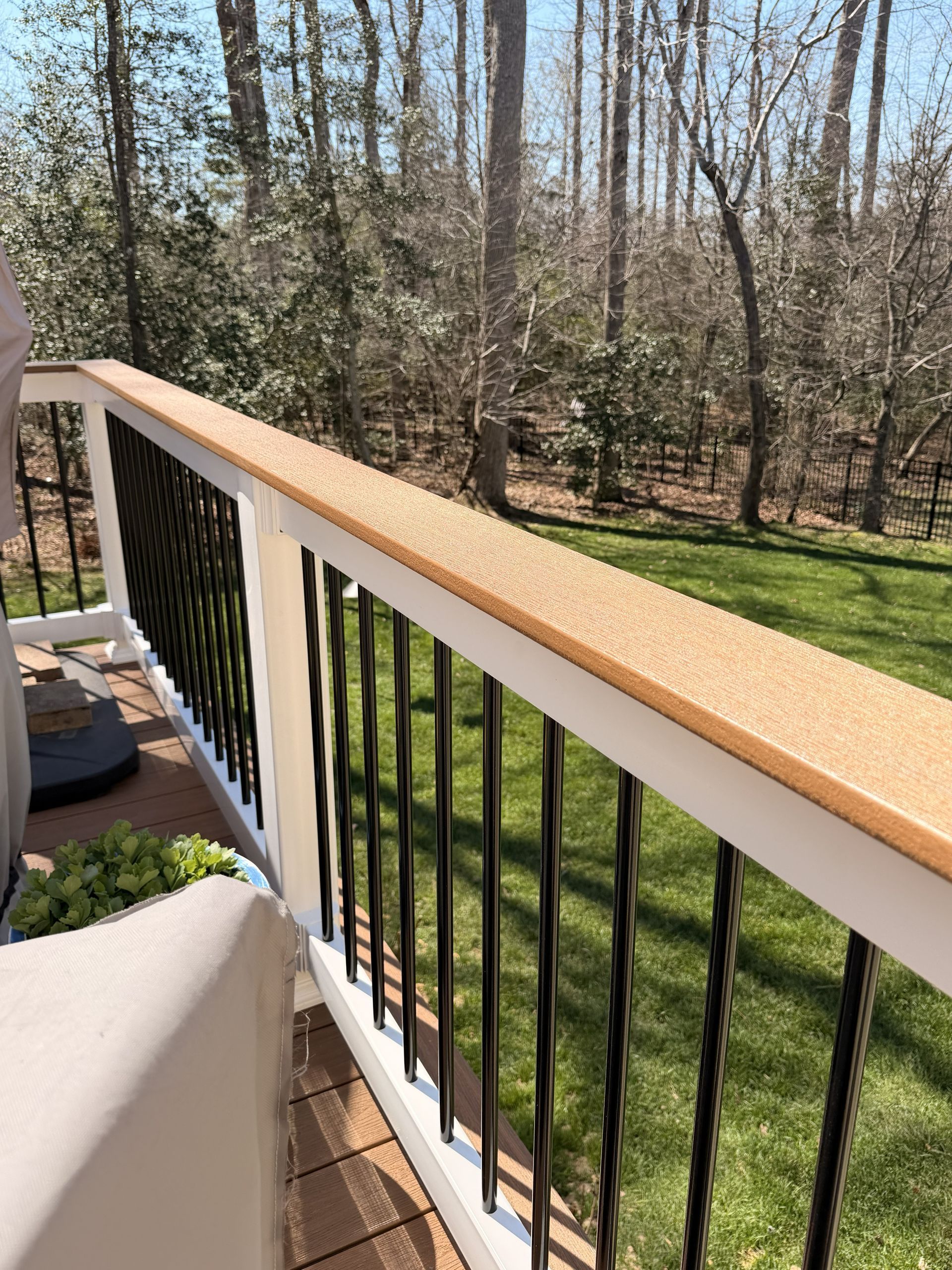 Wooden deck railing with black balusters overlooking a grassy yard and trees
